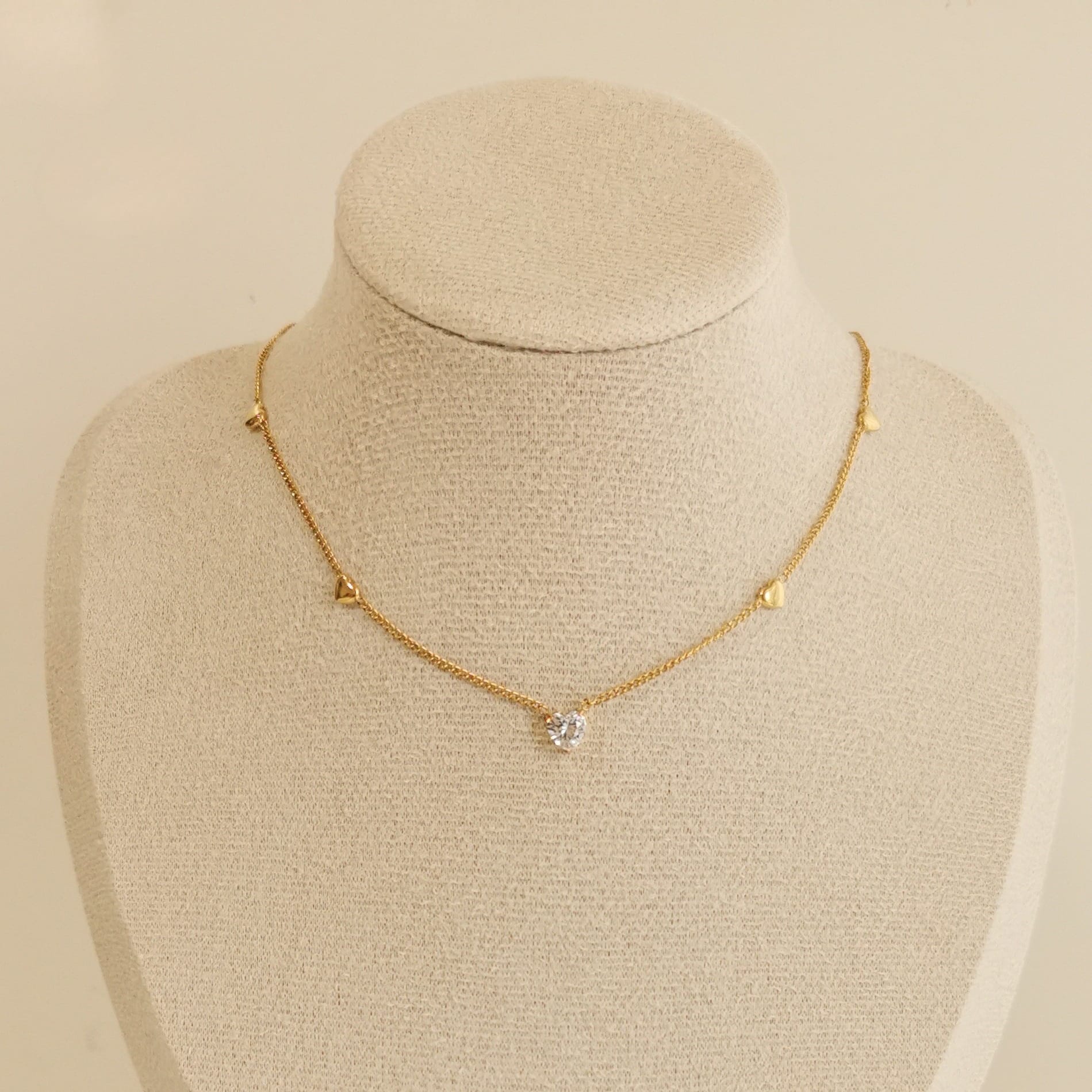 Vergoldete Herz Kette mit zentralem Zirkonia-Stein und kleinen Herzanhängern auf beiger Schmuckbüste